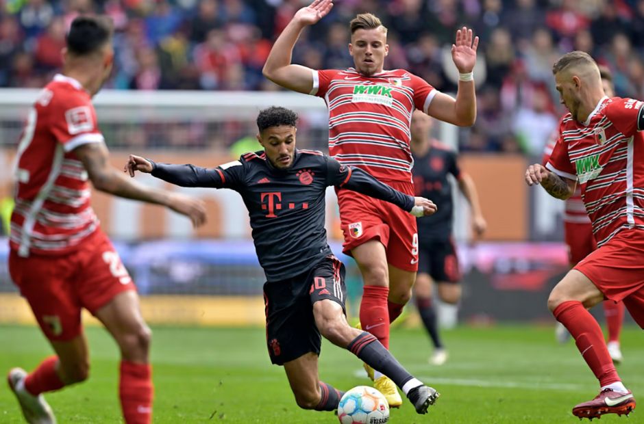 Các cầu thủ Augsburg trong trang phục màu đỏ đang vây công một cầu thủ của Bayern 
